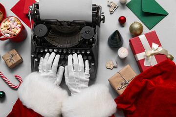 Santa Claus hands with Christmas decor, letters, gift boxes and cup of cacao typing on typewriter...