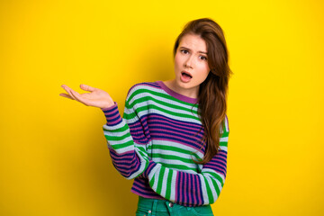 Young brunette woman in striped sweater on bright yellow background expresses confusion curiosity and surprise in a casual lifestyle shot