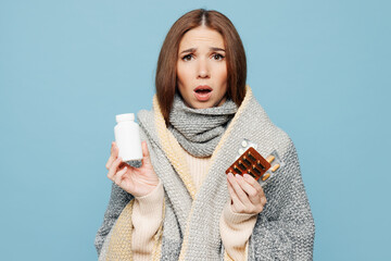 Young shocked sad scared woman wrapped in plaid holding multiple medication drug pill bottle...