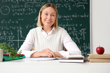 Mature female math teacher sitting at table with notebooks in classroom