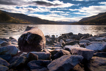 Rocky lake shore in Norway, with sparkling water and mountain views in autumn.