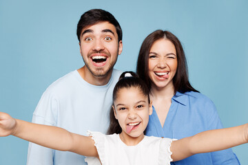 Fototapeta premium Close up young funny parents mom dad with child kid daughter girl wearing casual clothes do selfie shot on mobile cell phone isolated on plain blue background. Family day parenthood childhood concept.
