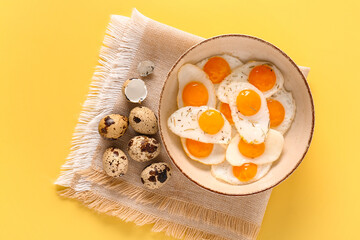 Bowl with fried quail eggs on yellow background