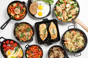 Frying pans with different tasty dishes on light background