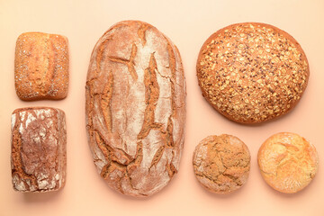 Loaves of fresh bread and buns on beige background