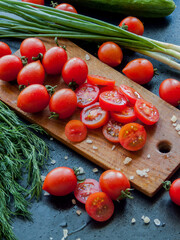 Fresh red cherry tomatoes with herbs and leek sprinkled with sea salt on wooden board on table, top view of vegetables covered with drops.
