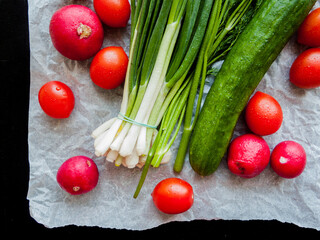 Fresh red cherry tomatoes, green leek, radish and cucumber on the parchment.
