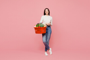 Full body young smiling cheerful woman wears white casual clothes hold orange basket bag with food products look camera isolated on plain pink background studio portrait. Delivery service from shop. © ViDi Studio