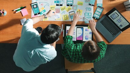 Top down view of manager working together to develop Ux Ui design for mobile interface. Developer partner working together discussing about changing software app while using on laptop. Convocation.