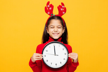 Merry little girl wear red clothes fun decorative deer horns on head posing hold in hands clock making wish isolated on plain yellow background. Happy New Year Christmas celebration holiday concept.