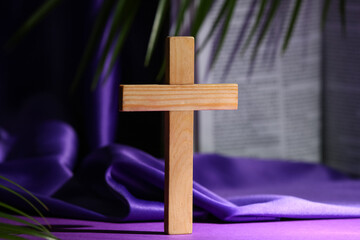 Wooden cross with Bible, palm leaf and purple cloth on color background. Good Friday concept
