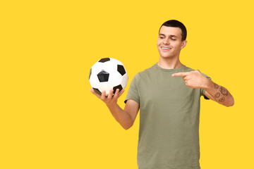 Handsome young man pointing at soccer ball on yellow background