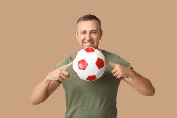 Handsome mature man pointing at soccer ball on brown background