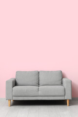Cozy grey sofa near pink wall