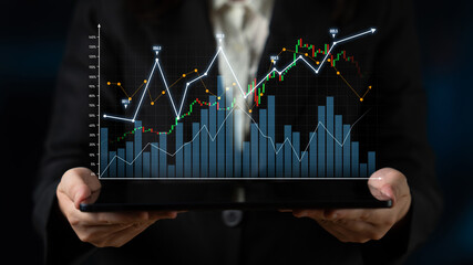 A businesswoman holds a tablet displaying dynamic financial charts and graphs indicating growth and market trends in a dark setting, emphasizing digital analytics. Scalp