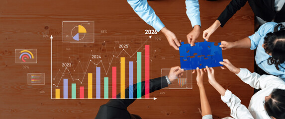 Group of diverse professionals collaborating to solve a puzzle while analyzing business growth trends with visual data representations for strategic planning. Trope