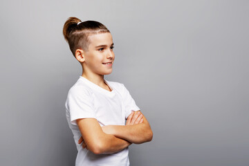 Stylish young boy posing in studio with trendy shaved sides and sleek ponytail hairstyle, smiling with arms crossed, modern fashion portrait on clean gray background
