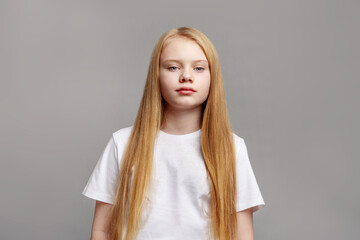 Beauty portrait young blond girl with long straight hair and blue eyes in studio, posing on gray background in modern minimal style. Caucasian Fashion model in white clothing looking at camera