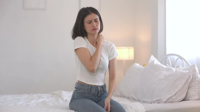 women sitting on bed with painful expression, holding her shoulder due to muscle pain or stiffness. Concept of body ache, muscle strain, poor posture or sleep discomfort.