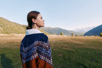 Naklejka premium Woman portrait in sweater profile standing in a meadow with mountains and valley in background, outdoors nature scene showing calm horizon, serene expression and scenic landscape.