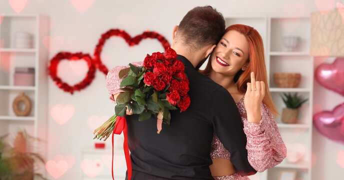 Beautiful young happy couple with bouquet of roses and engagement ring at home. Valentine's Day celebration - Powered by Adobe
