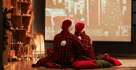Young couple watching Christmas movie on projector screen at home, back view