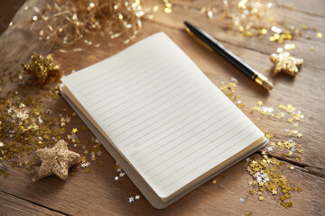 open lined notebook surrounded by scattered gold glitter and decorative stars on natural wooden surface, cozy creative setup, concept of stationery promotion and festive storytelling
