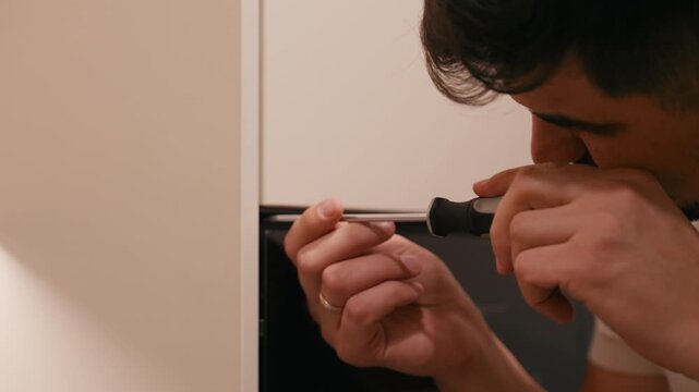 Skilled man using a screwdriver to fix a cabinet door, showcasing detailed craftsmanship, with a gradual zoom in on the intricate work being performed