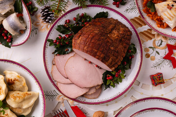 Classic Christmas food medley on a decorated table. Fish, dumplings stuffed with cabbage and mushrooms, cheesecake, and ham.