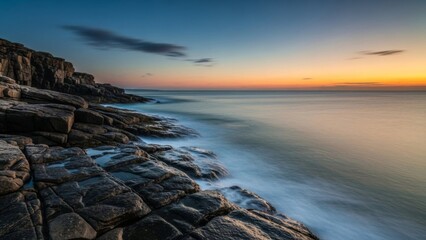 Serene long exposure view of a rugged rocky coastline at twilight, featuring blurred ocean waves and a vibrant gradient sky.