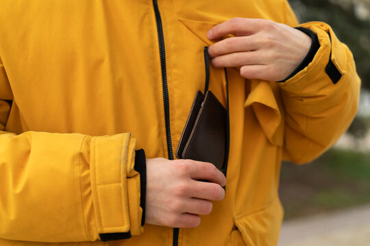 A person inserts a wallet into the pocket of a jacket while outdoors in winter