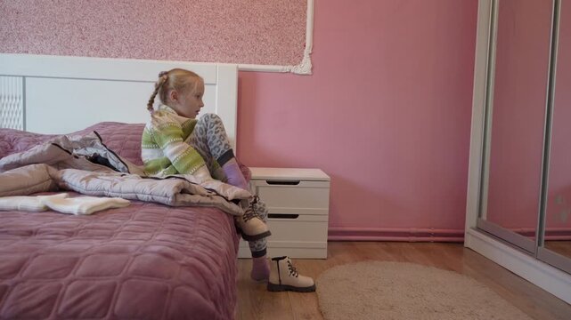 child putting on shoes on edge of bed, little girl getting ready to leave home putting on white shoes, Child sitting on bed putting on shoes.