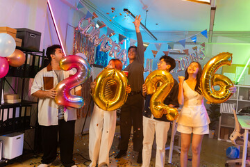 Asian business team celebrating New Year 2026 or major milestone achievement in office party,holding large 2026 foil number balloons and confetti falling.Concept of corporate success,festive teamwork 