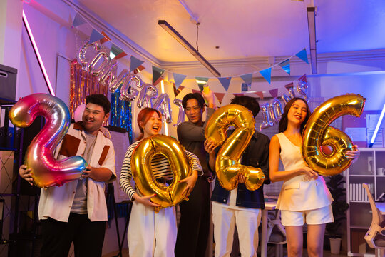 Asian business team celebrating New Year 2026 or major milestone achievement in office party,holding large 2026 foil number balloons and confetti falling.Concept of corporate success,festive teamwork 