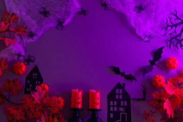 Halloween flat lay background with a frame of pumpkins, spiders, bats, and haunted houses, illuminated by purple lighting.
