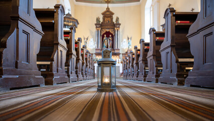 A lantern holding the Bethlehem light stands on the floor of a church. The surrounding wooden pews...
