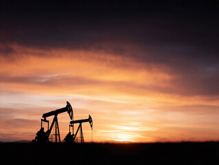 Silhouette of oil pumps against a vibrant sunset. Evokes themes of energy, industry, and the environment. Ideal for articles, reports, and web designs.