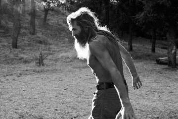 Black and white photo of shirtless bearded man walking outdoors in forest