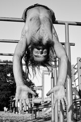 Shirtless man hanging upside down on metal bars in black and white photo