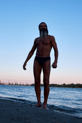 Silhouette of a bearded man standing on the beach by the water at sunset