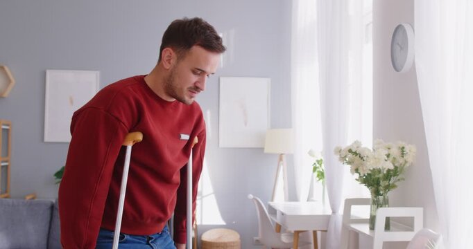 Man with trauma walking using crutches at home, broken leg, patient after accident, traumatic stress, accident, injured adult having problem with balance, muscle weakness, injury, bad pain in legs