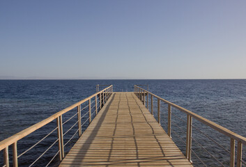 Obraz premium Wooden pier leading into the calm blue sea under clear sky 