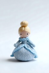 Handmade knitted princess doll in blue dress with blonde hair bun isolated on white background for crafts and children toys.