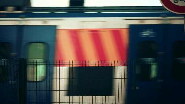 Blurred train passing behind a metal fence, creating an abstract transportation scene with strong graphic lines