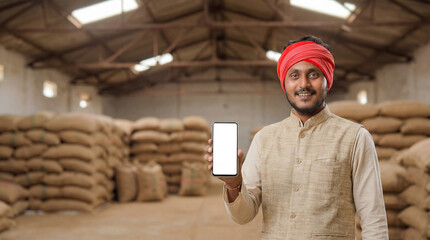 Smiling Indian Farmer Shows Smartphone in Grain Storage Warehouse