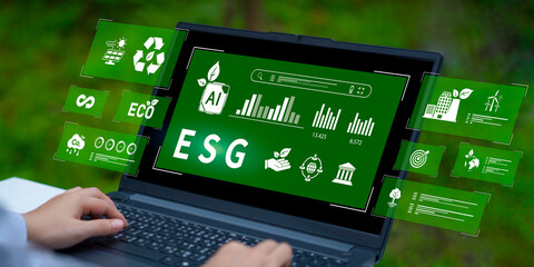 Hand interacting with digital overlay showing ESG framework, renewable energy, and data analytics on a computer screen against a natural backdrop.
