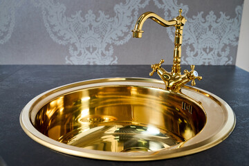 Kitchen luxurious interior with golden brass round sink basin and faucet double tap mixer in contemporary modern design with stone marble stoneware countertop.