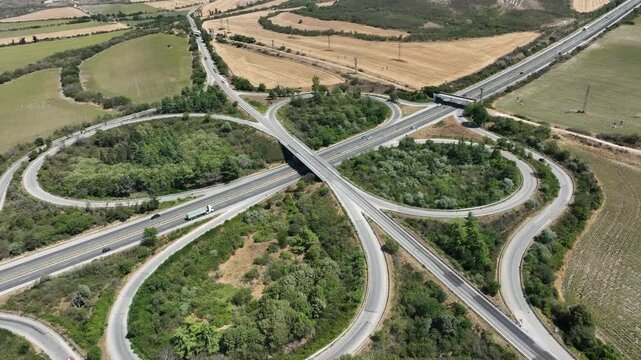 Aerial view of a symmetrical cloverleaf highway interchange. Cars on the road network show transportation and logistics in a rural landscape, symbolizing connectivity and infrastructure.