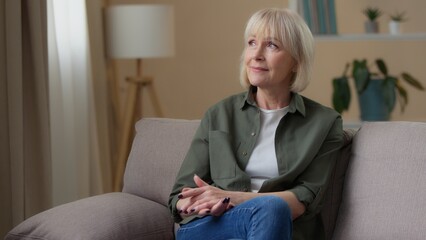Pensive dreaming thoughtful elderly old Caucasian woman looking away at home relaxing on couch mature retired female look in window on sofa thinking senior lady grandma contemplate pondering indoors