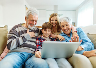 Family grandparents and grandchildren having fun at home using laptop